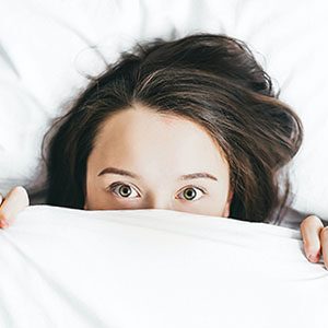 woman suffering insomnia peeking over the bed covers wide eyed